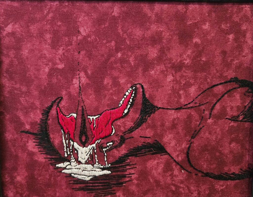 A photograph of an embroidered image on marbled magenta fabric. The image is of a nude body, lying on its back. The focus is on the face, which has been hollowed out by a flame like a candle. Wax or fat or brain matter drips and pools on the ground.